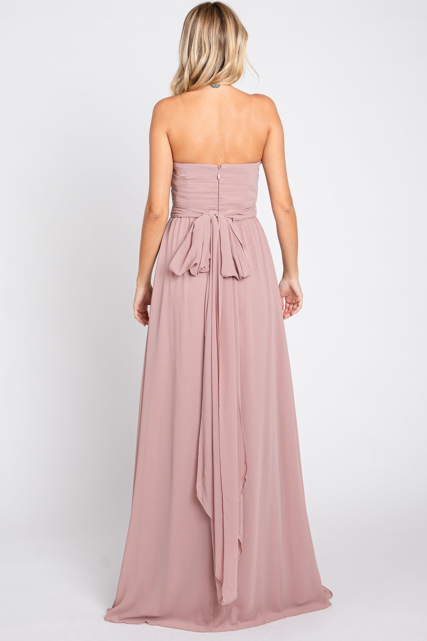 woman wearing a blush strapless maxi dress with a tied bow detail at the back
