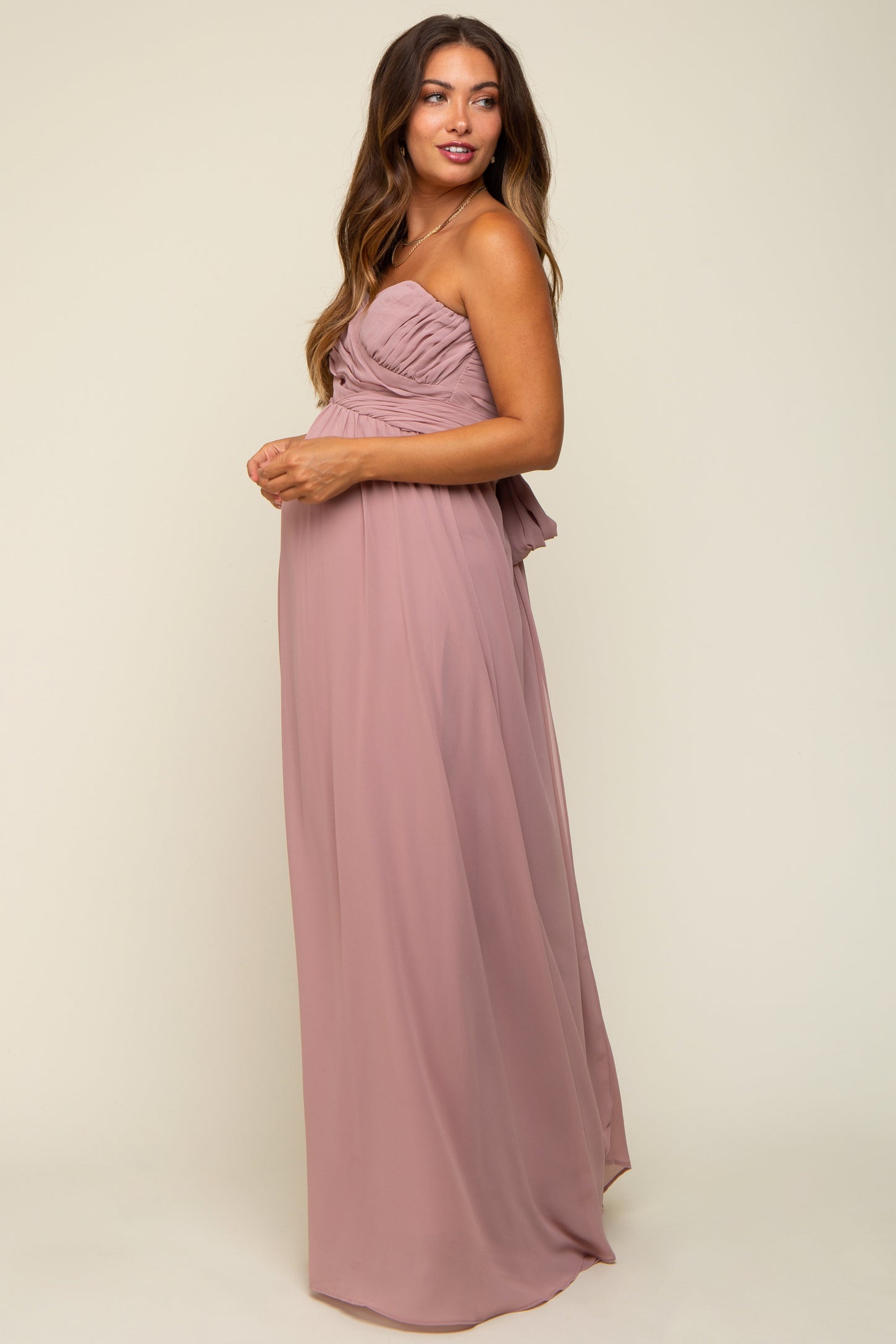 woman wearing a blush pink maternity gown with ruched bodice and flowy skirt, showcasing a baby bump
