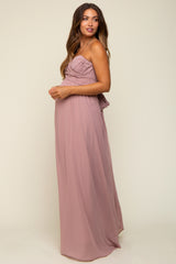 woman wearing a blush pink maternity gown with ruched bodice and flowy skirt, showcasing a baby bump