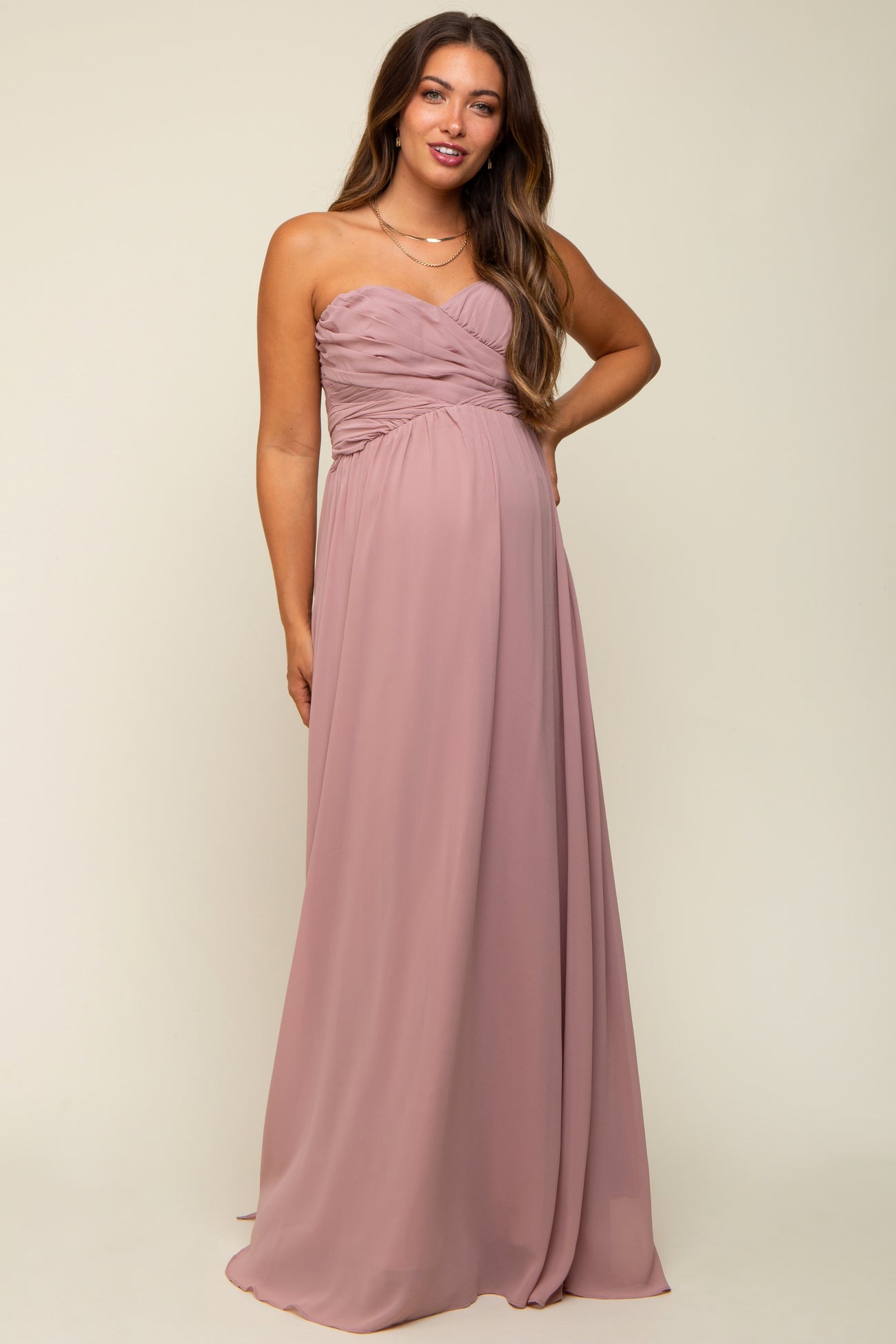 woman wearing a strapless mauve maternity gown with a ruched bodice and flowing skirt, showcasing her baby bump