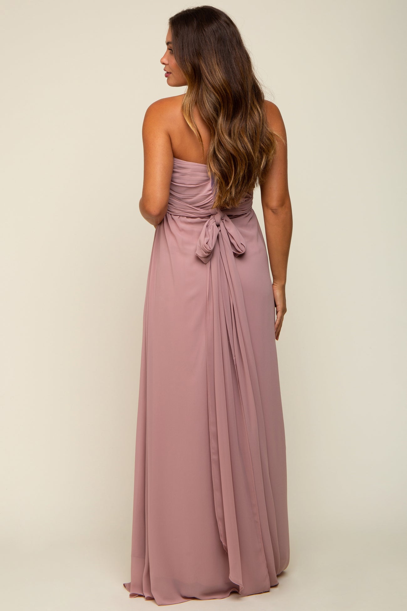 woman wearing a blush strapless maternity gown with a tied back detail, showing flowing fabric and a relaxed fit