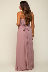 woman wearing a blush strapless maternity gown with a tied back detail, showing flowing fabric and a relaxed fit