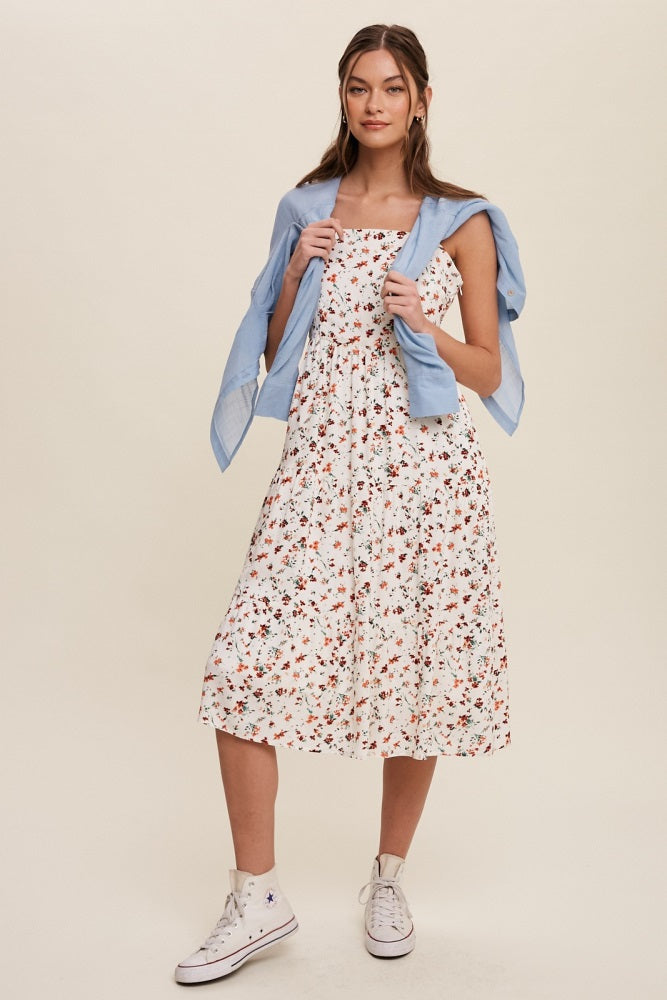 woman wearing a white floral midi dress with a tied blue shirt and white sneakers