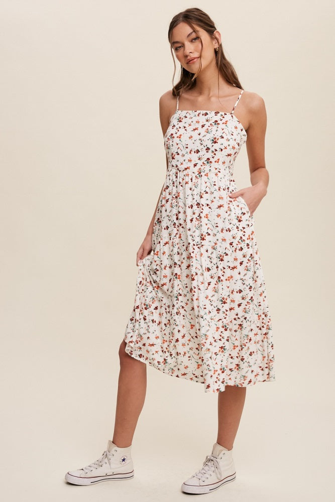 woman wearing a white floral midi dress with spaghetti straps and pockets, paired with white high-top sneakers