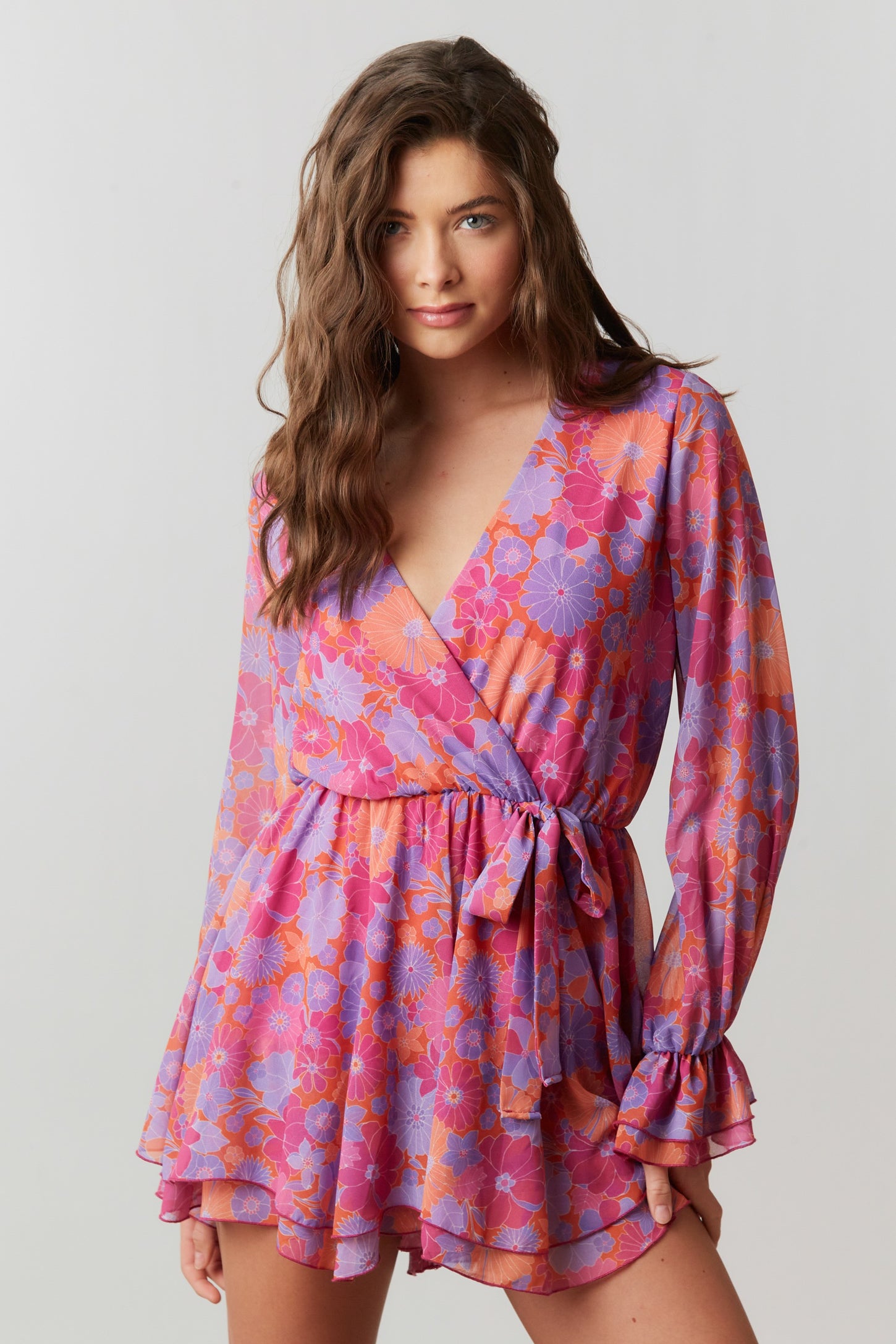 woman wearing a vibrant pink and purple floral wrap dress with long sleeves and a tie waist detail