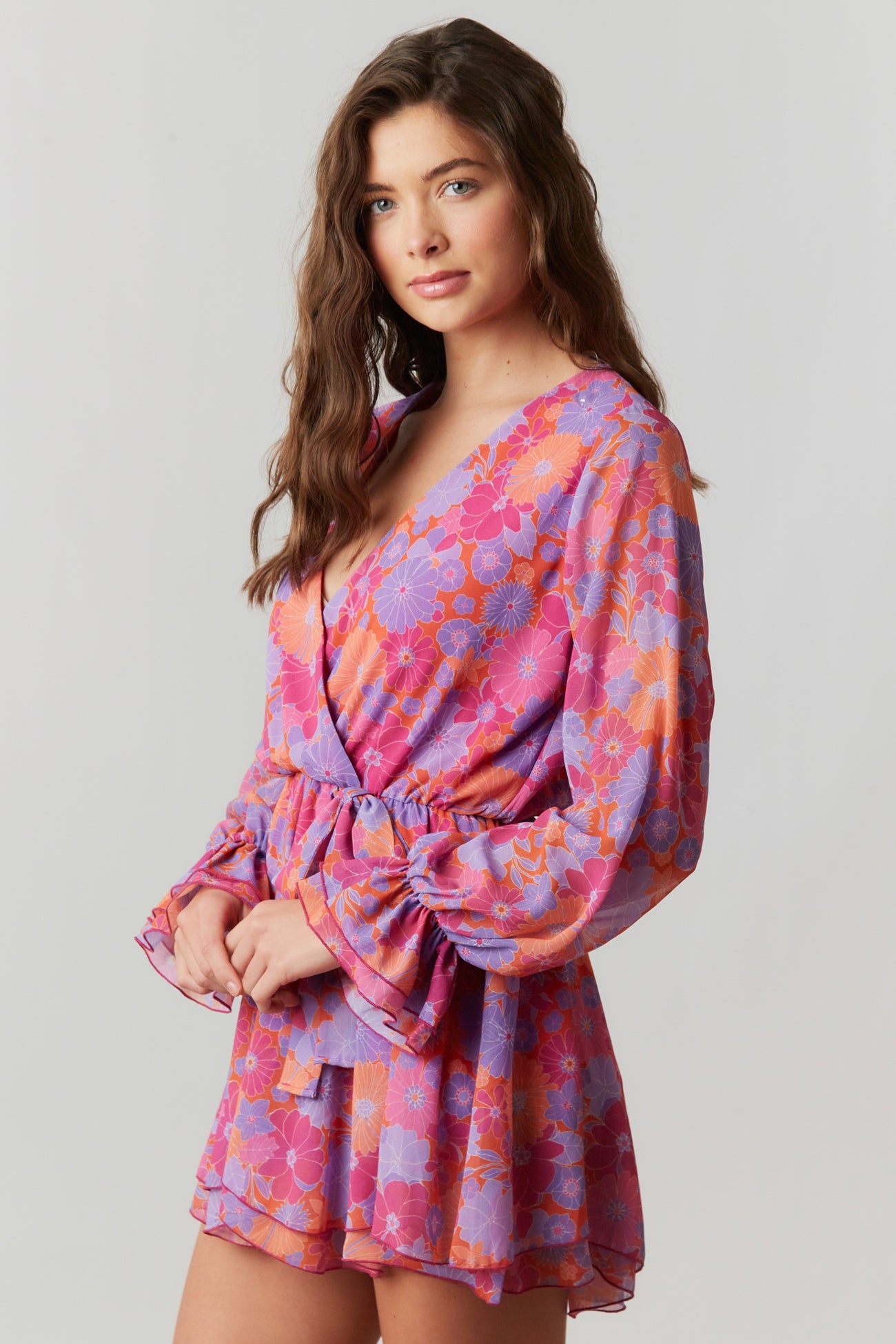 woman wearing a purple and pink floral print romper with long bell sleeves and a waist tie