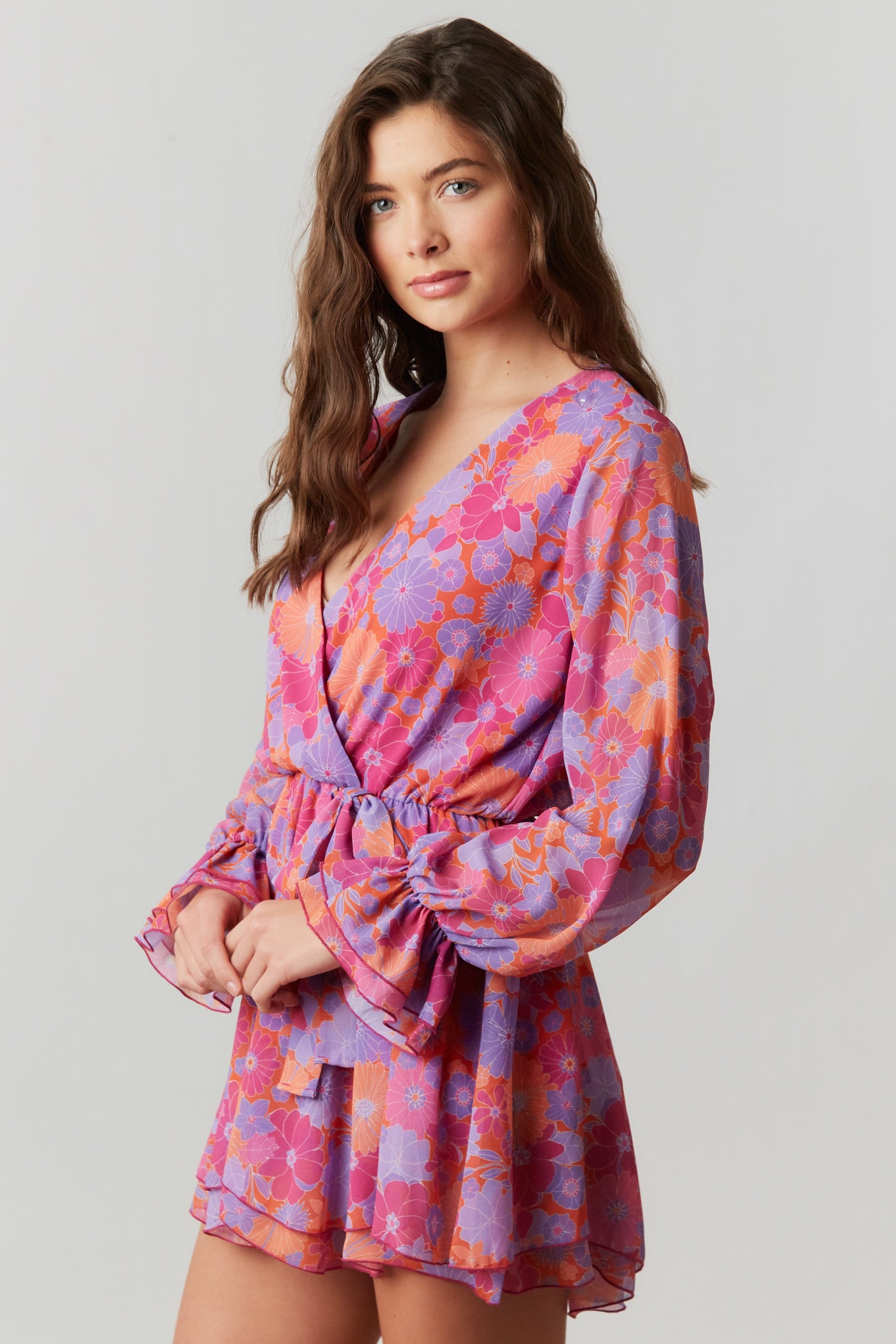 woman wearing a purple and pink floral print romper with long bell sleeves and a waist tie