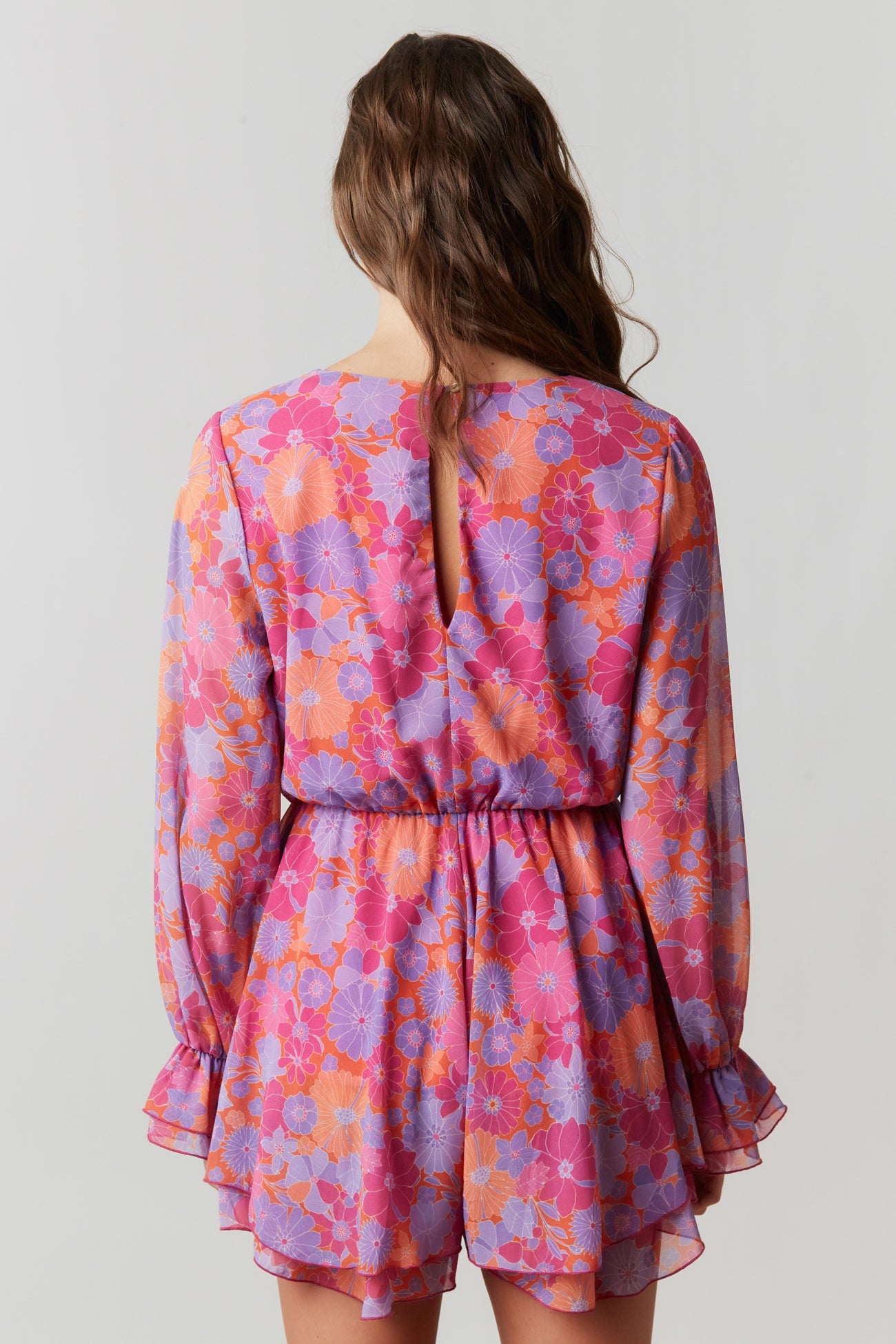 back view of a woman wearing a vibrant pink and purple floral mini dress with long sleeves and a keyhole detail