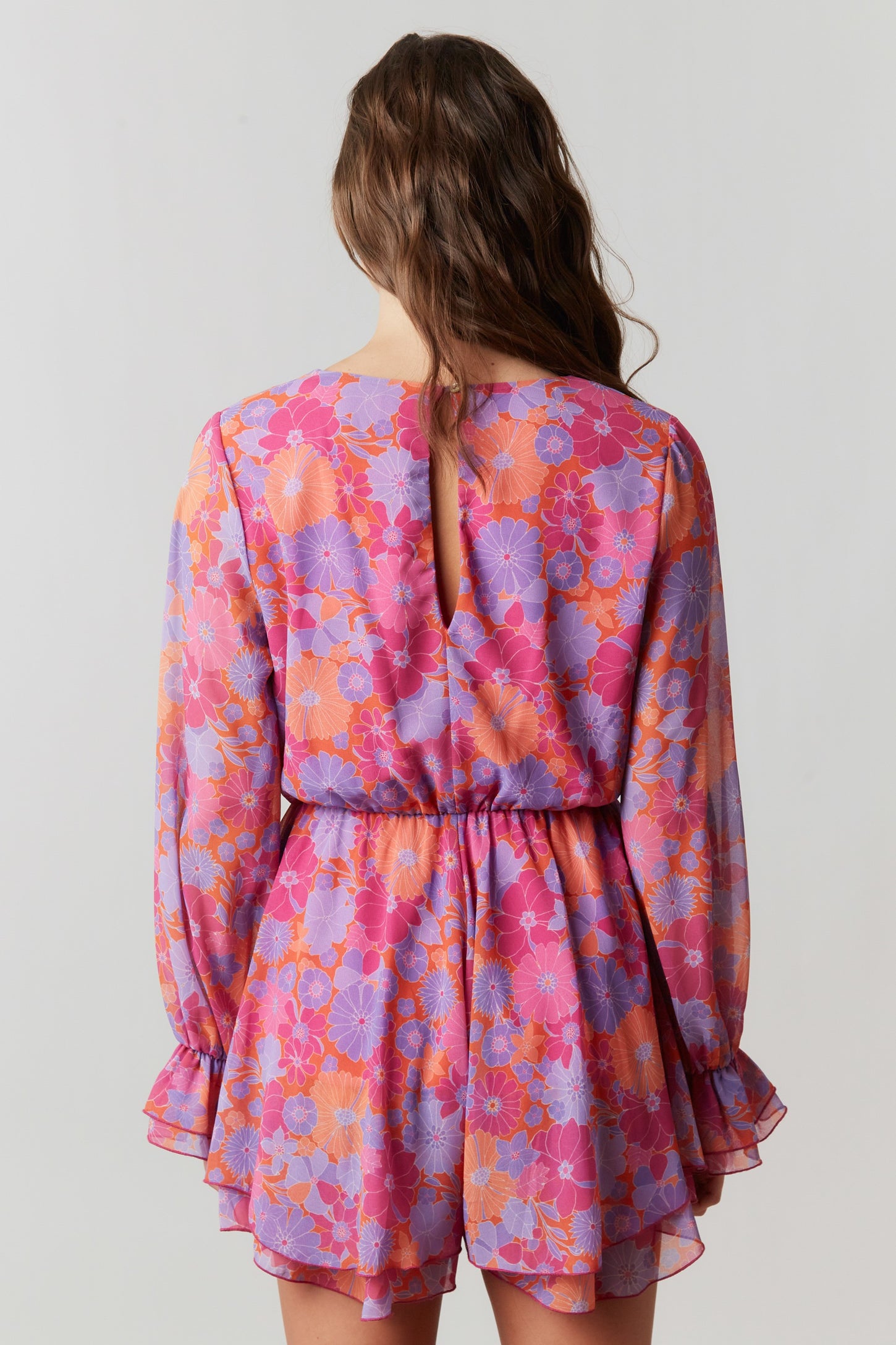 back view of a woman wearing a vibrant pink and purple floral mini dress with long sleeves and a keyhole detail
