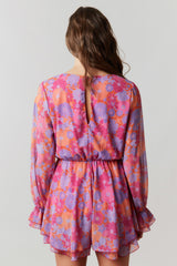 back view of a woman wearing a vibrant pink and purple floral mini dress with long sleeves and a keyhole detail