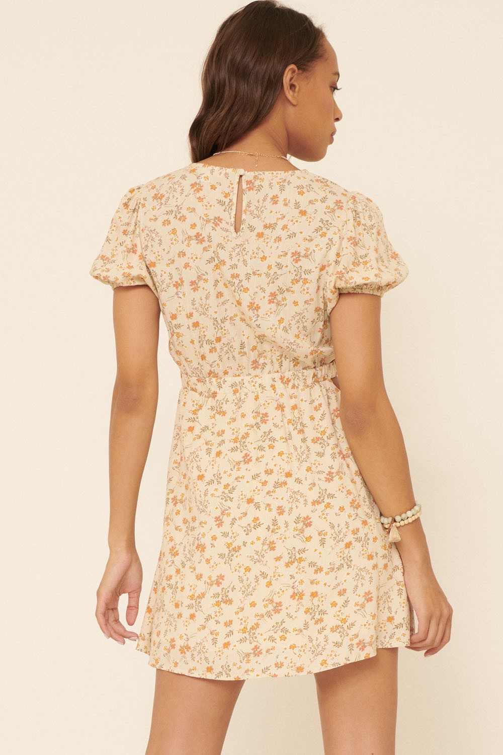 woman wearing a beige floral print short dress with puff sleeves and a keyhole detail at the back