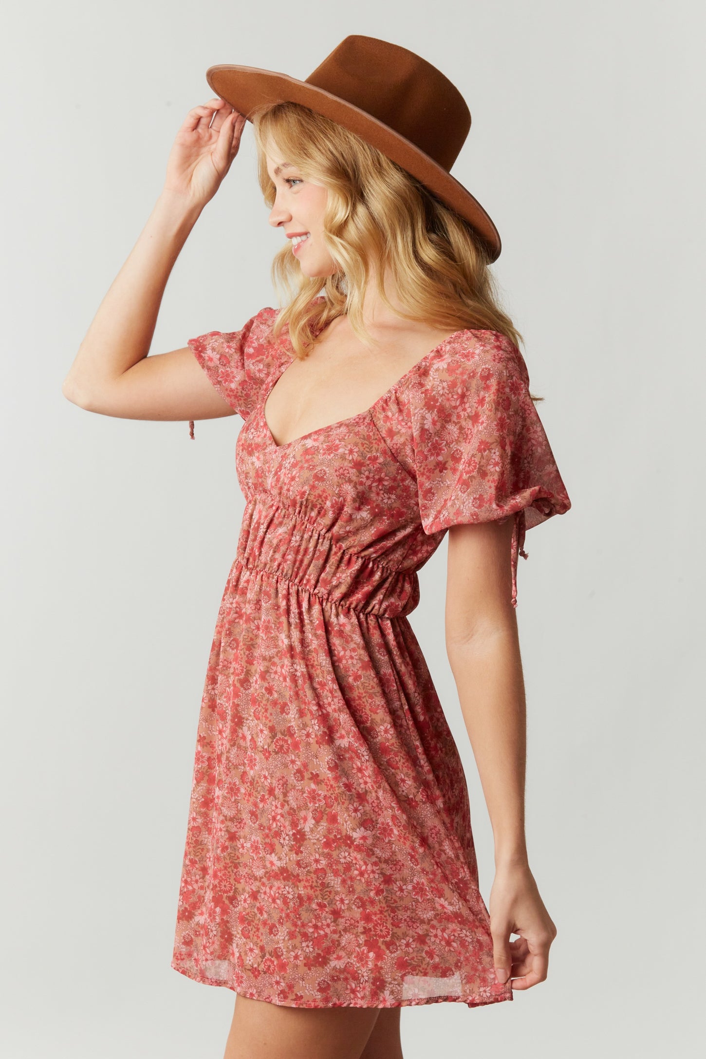 woman wearing a pink floral print dress with puff sleeves and cinched waist, styled with a wide-brimmed hat