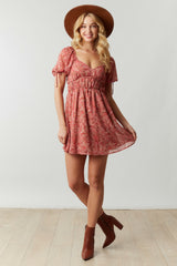 woman wearing a pink floral mini dress with puff sleeves and a cinched waist, paired with a wide-brimmed hat and ankle boots