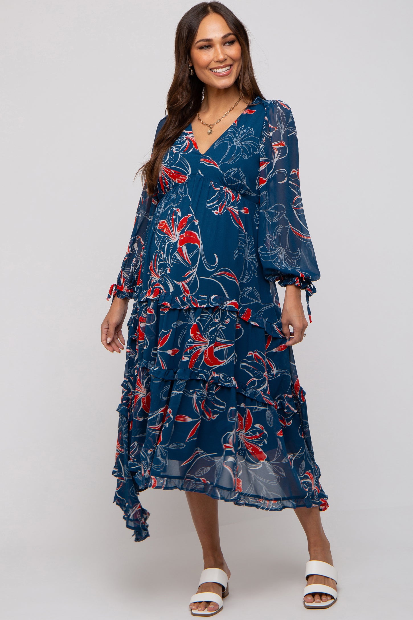 woman wearing a navy floral maternity dress with tiered ruffle detail and long sleeves, showing her baby bump