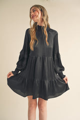 woman wearing a black long sleeve tiered dress with ruffle details and a mock neck