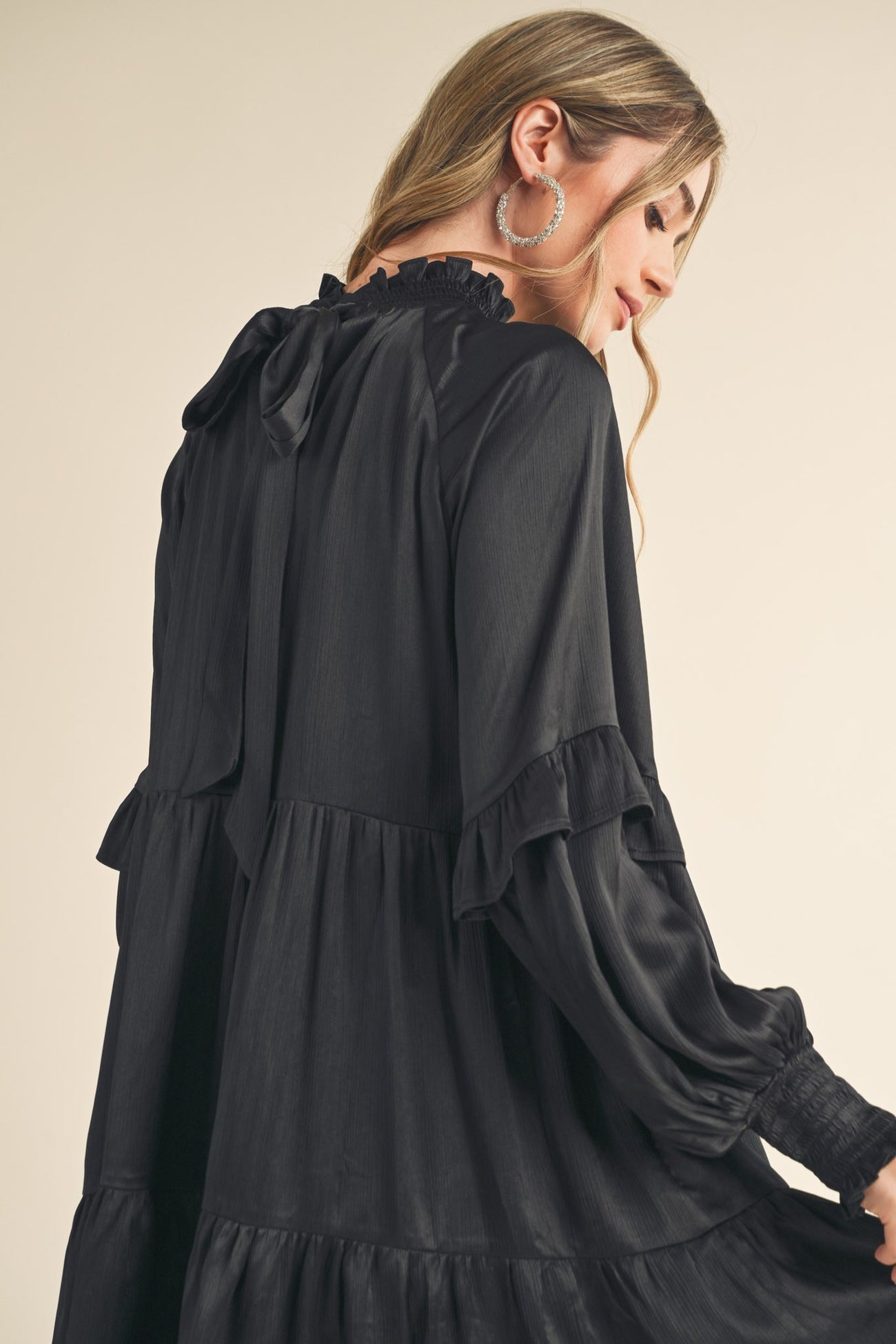 woman wearing a black long sleeve ruffled dress with a tie at the neck and a tiered skirt