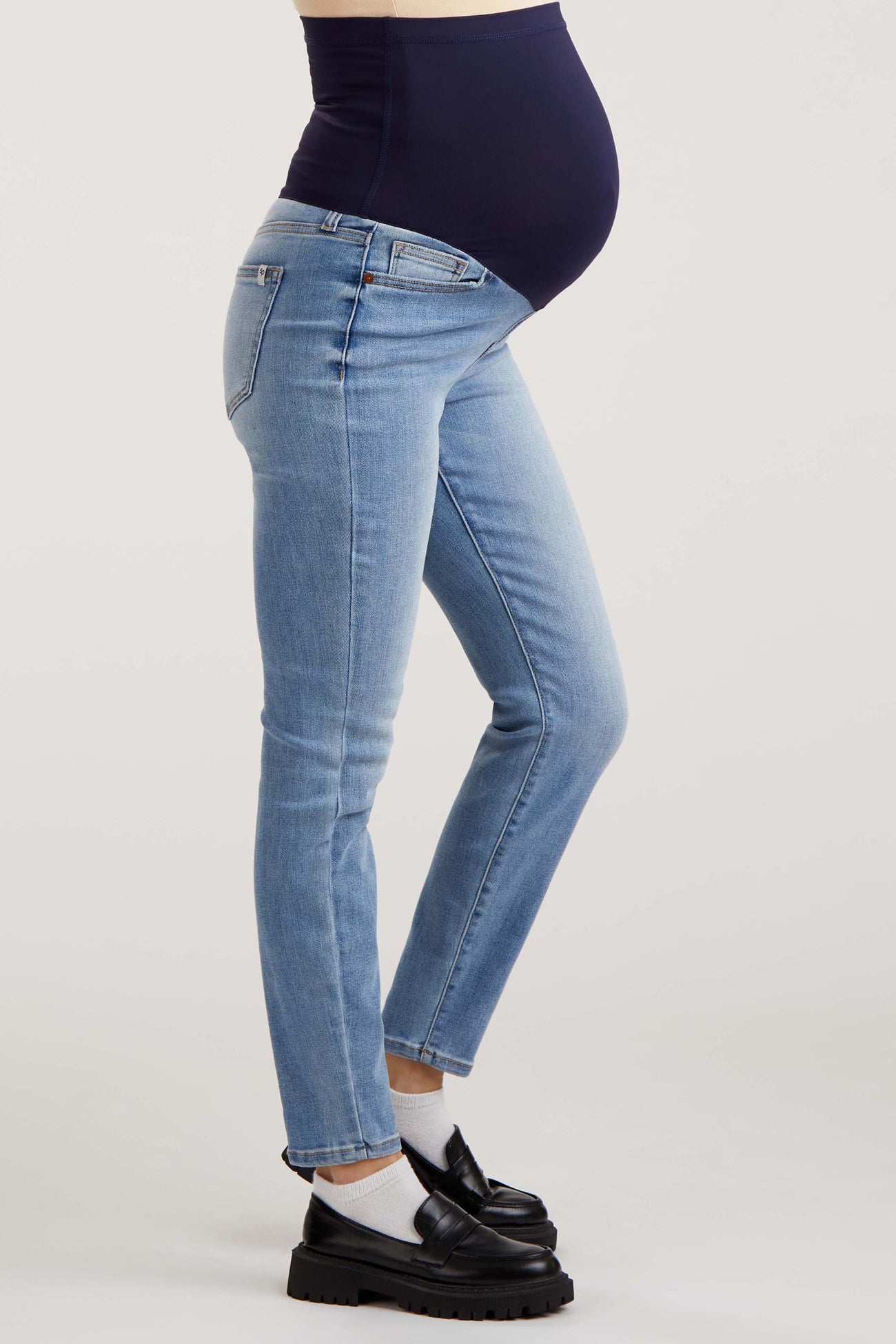 woman wearing light blue maternity jeans with a dark blue over-the-bump panel and visible baby bump