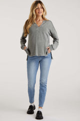 woman wearing a gray long sleeve maternity top with v-neck and side slits, paired with blue jeans and black slip-on shoes