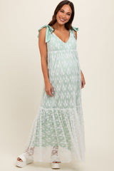 woman wearing a mint green maternity maxi dress with lace detailing and tie straps, showing her baby bump