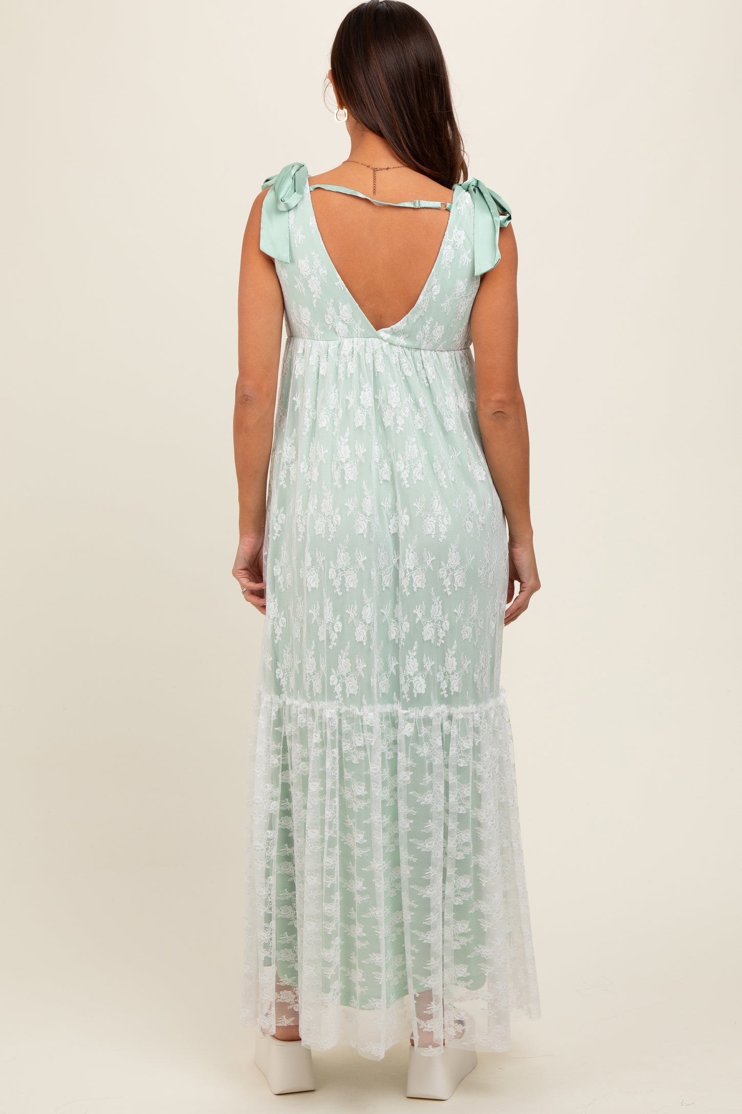 woman wearing a mint green floral maternity dress with lace details and tie straps, showing a baby bump from the back
