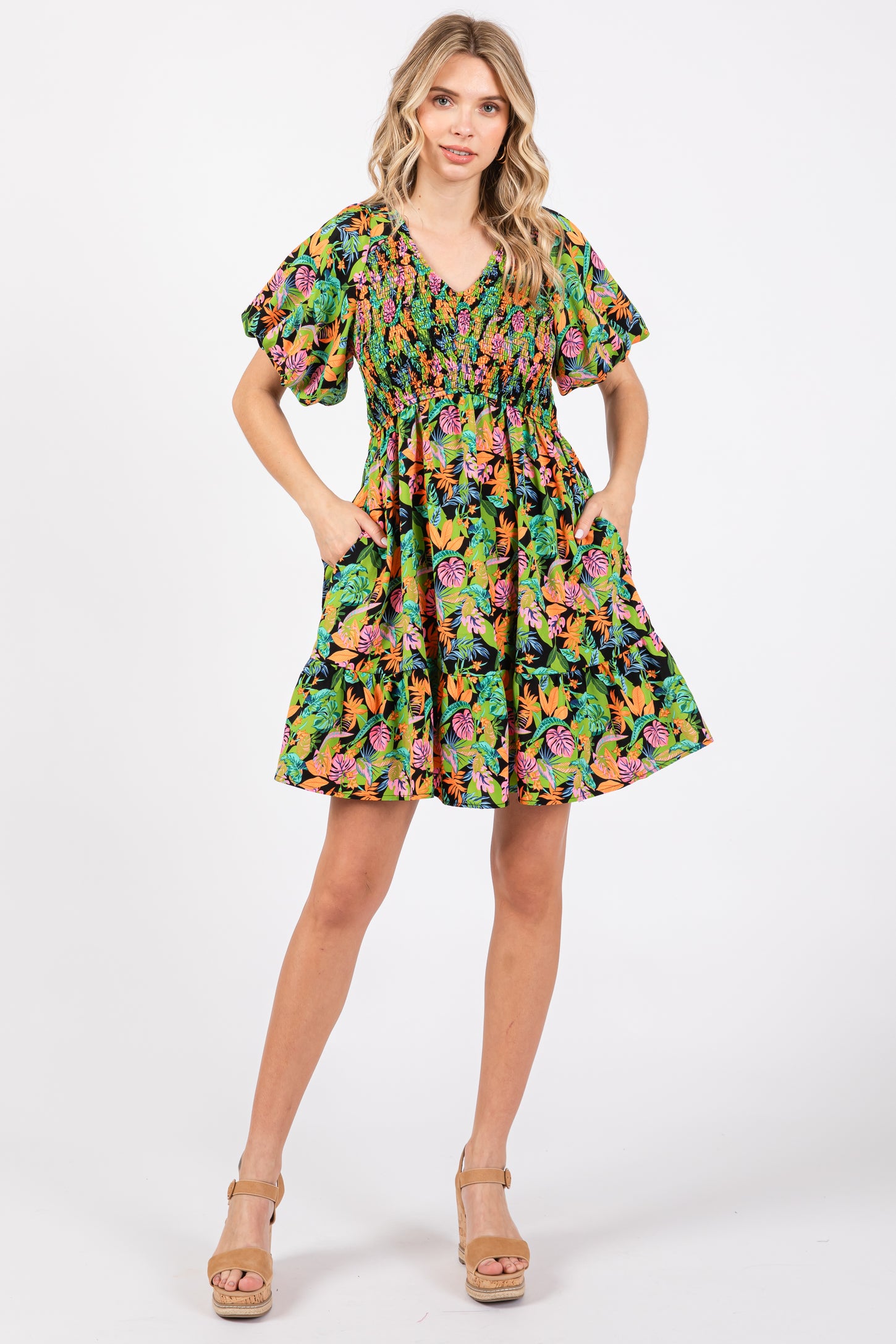 woman wearing a vibrant green floral short dress with puff sleeves and pockets, standing in a relaxed pose