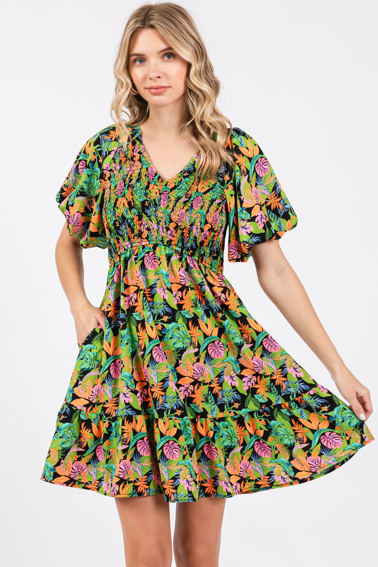 woman wearing a vibrant floral print short dress with puff sleeves and a smocked bodice, posing with one hand on her waist