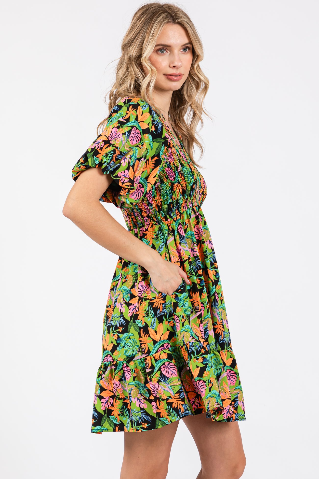 woman wearing a black tropical print puff sleeve dress with a smocked bodice and pockets