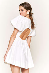 woman wearing a white puff sleeve mini dress with an open back and flowing skirt