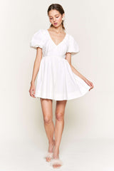 woman wearing a white short puff sleeve dress with a deep V-neck and flowing skirt