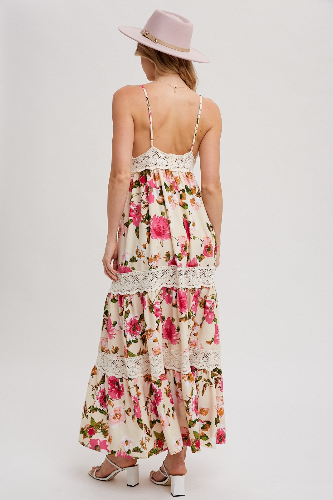 woman wearing a floral maxi dress with lace details and a tiered skirt, standing with a pink hat on her head