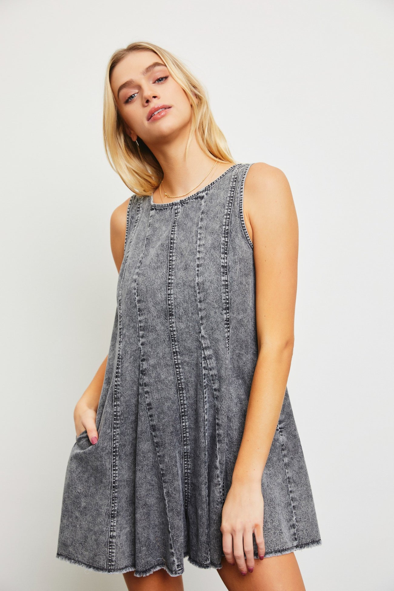 woman wearing a gray denim sleeveless mini dress with a slightly flared silhouette and pocket details