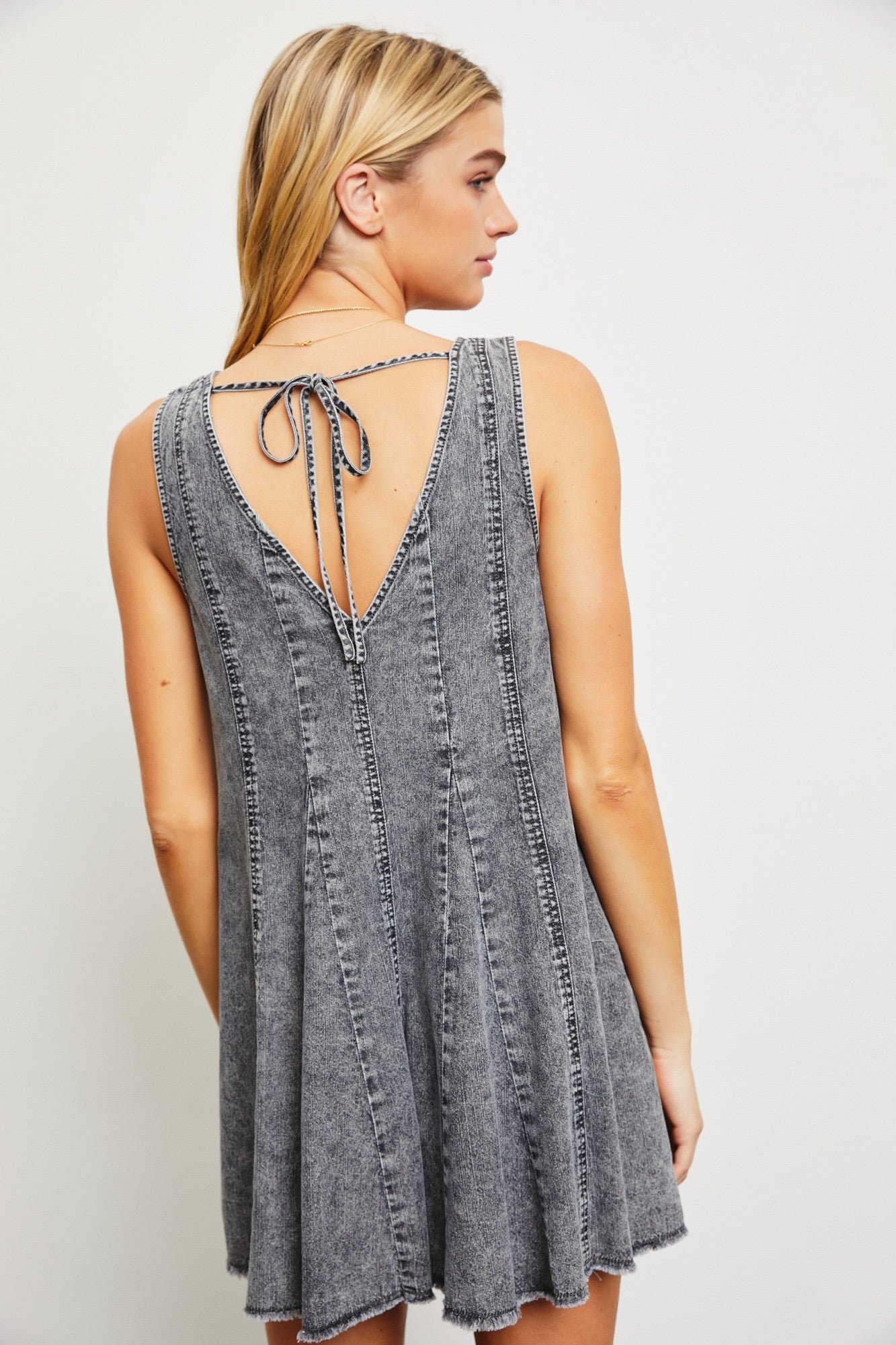 woman wearing a gray sleeveless denim dress with a tie-back detail and a skater-style silhouette