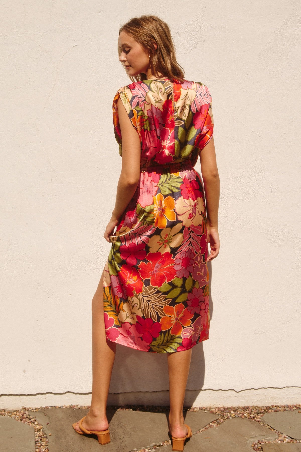 woman wearing a colorful floral midi dress with short sleeves and a side slit, standing against a white wall
