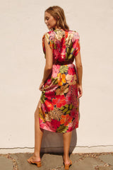 woman wearing a colorful floral midi dress with short sleeves and a side slit, standing against a white wall
